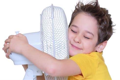 HVAC services in Butts County, Georgia - Young Boy in Butts County, Georgia trying to cool off in front of a fan while waiting for the technician from Reynaud HVAC Contractors to arrive and fix the AC system.